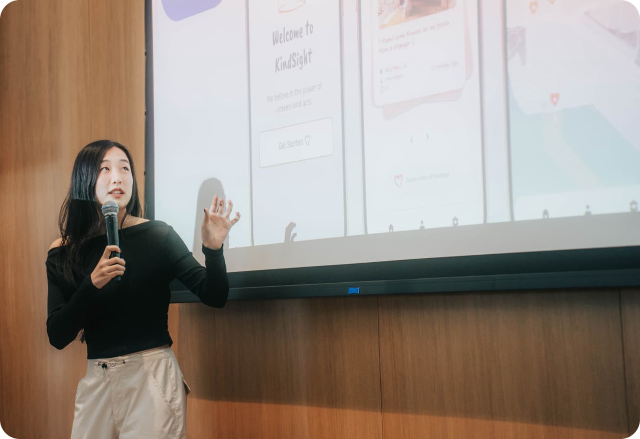 Alice gesturing at a presentation screen showing mobile mockups.