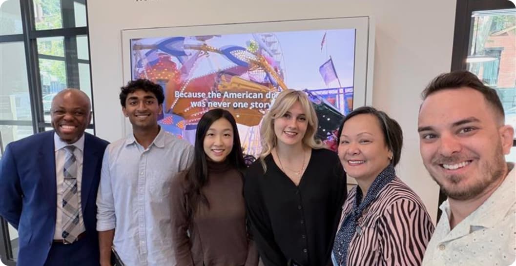 Six people posing together in front of a screen reading “Because the American dream was never one story,” during a branch visit.
